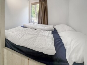 A bedroom with a bed, a window with curtains, and a view of trees outside. - Nice 8-person house in a child-friendly park. (Otterlo)