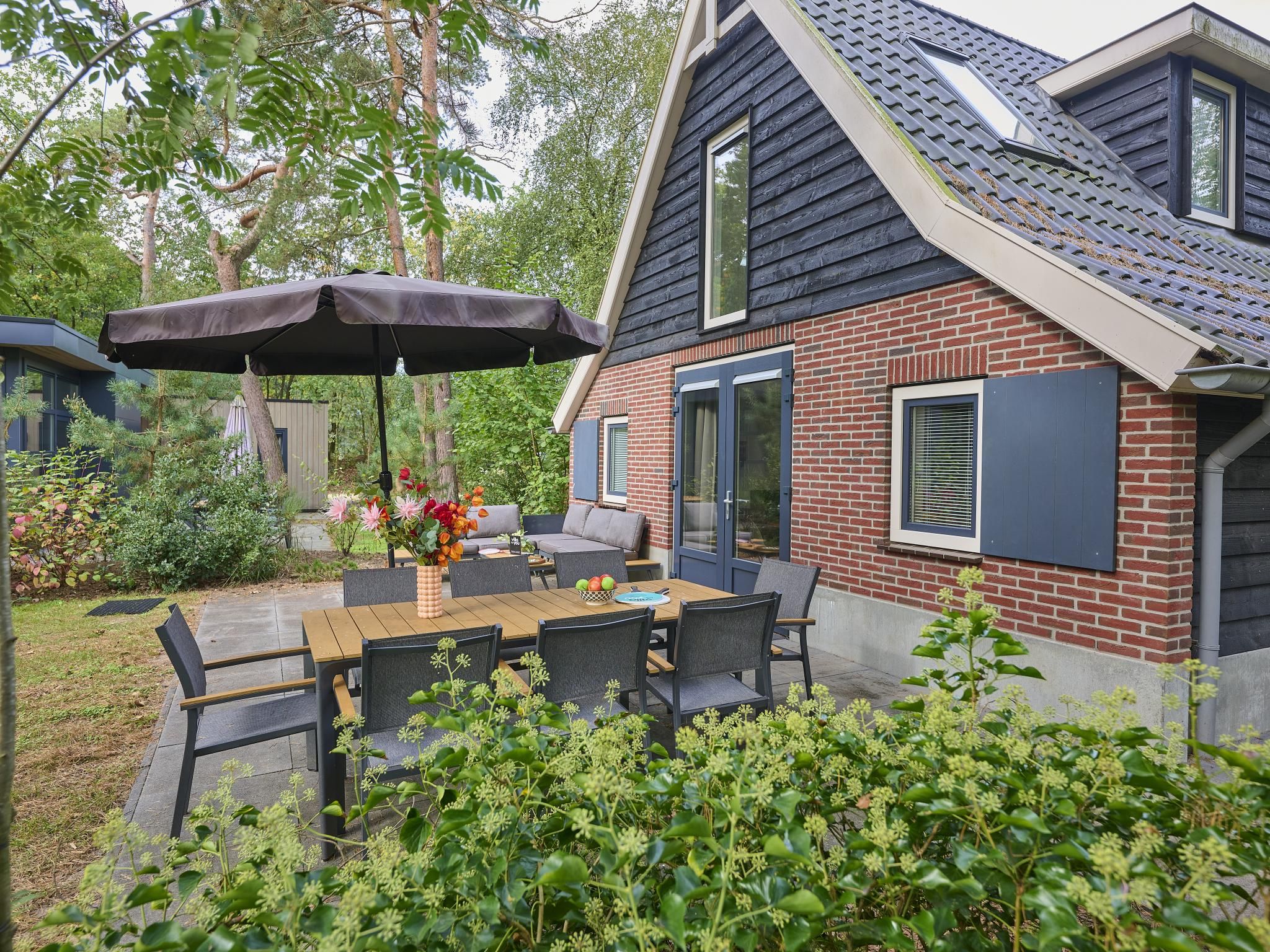 A patio with a table and chairs, a covered umbrella, and a brick house with a window.