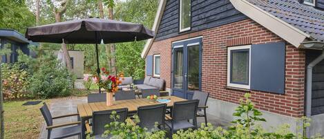 A patio with a table and chairs, a covered umbrella, and a brick house with a window.