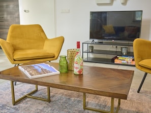 A living room with a wooden coffee table, two yellow armchairs, a green vase, a patterned bottle, and a magazine. - Nice 8-person house in a child-friendly park. (Otterlo)