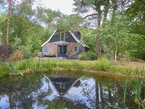 A house with a pond in front, surrounded by trees. - Nice 8-person house in a child-friendly park. (Otterlo)