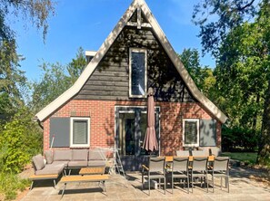 A house with a gabled roof, a brick exterior, and a patio with outdoor furniture. - Nice 8-person house in a child-friendly park. (Otterlo)