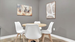 A dining area with a round table and white chairs, gray walls, and two artworks. - Dallas: Walk to Texas A&M Campus, Comfy King Beds (Bryan)
