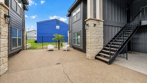 A building with a covered outdoor area, a staircase, and a blue building in the background. - Dallas: Walk to Texas A&M Campus, Comfy King Beds (Bryan)