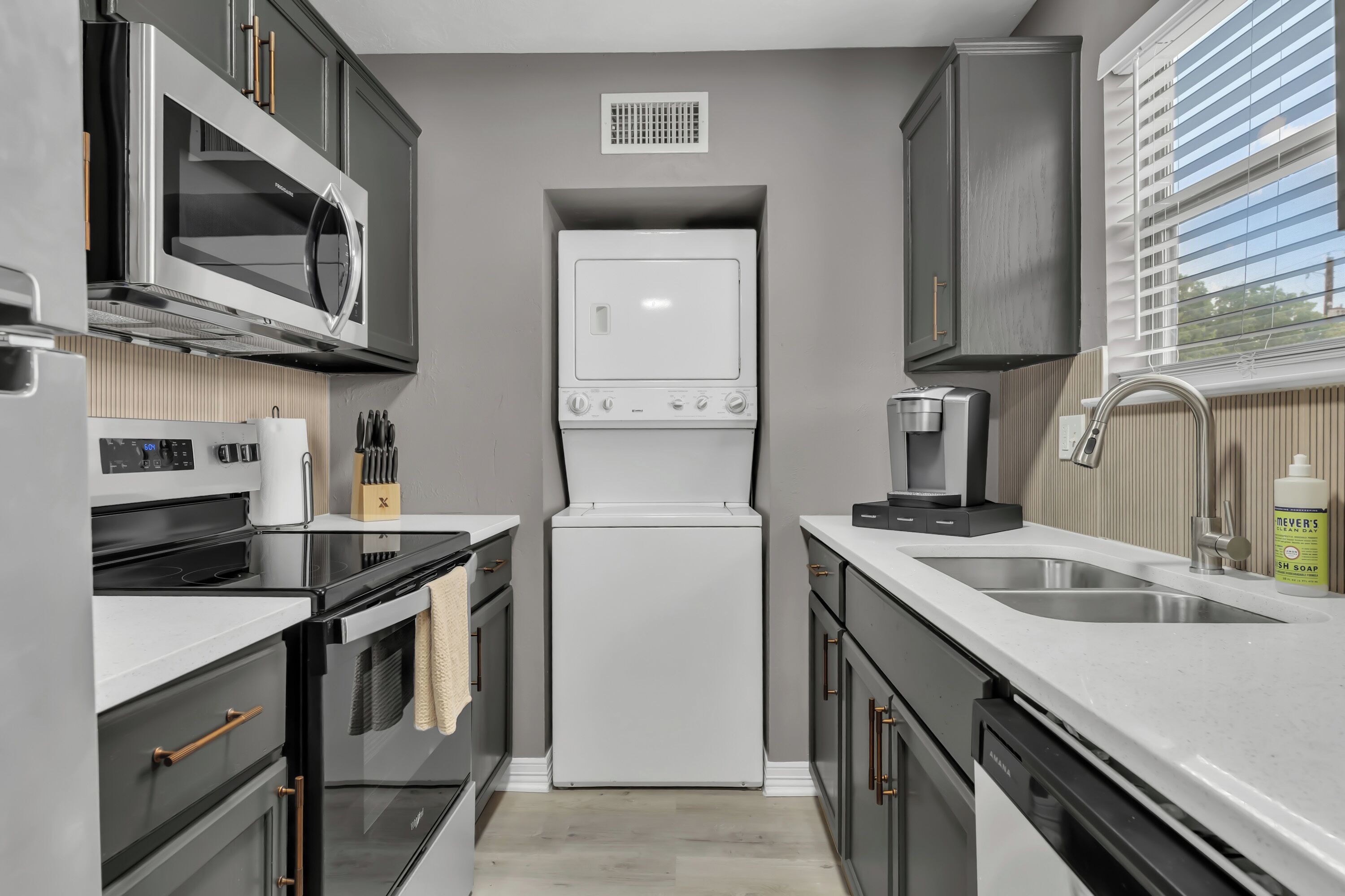 A modern kitchen with a microwave, oven, refrigerator, sink, and coffee maker.
