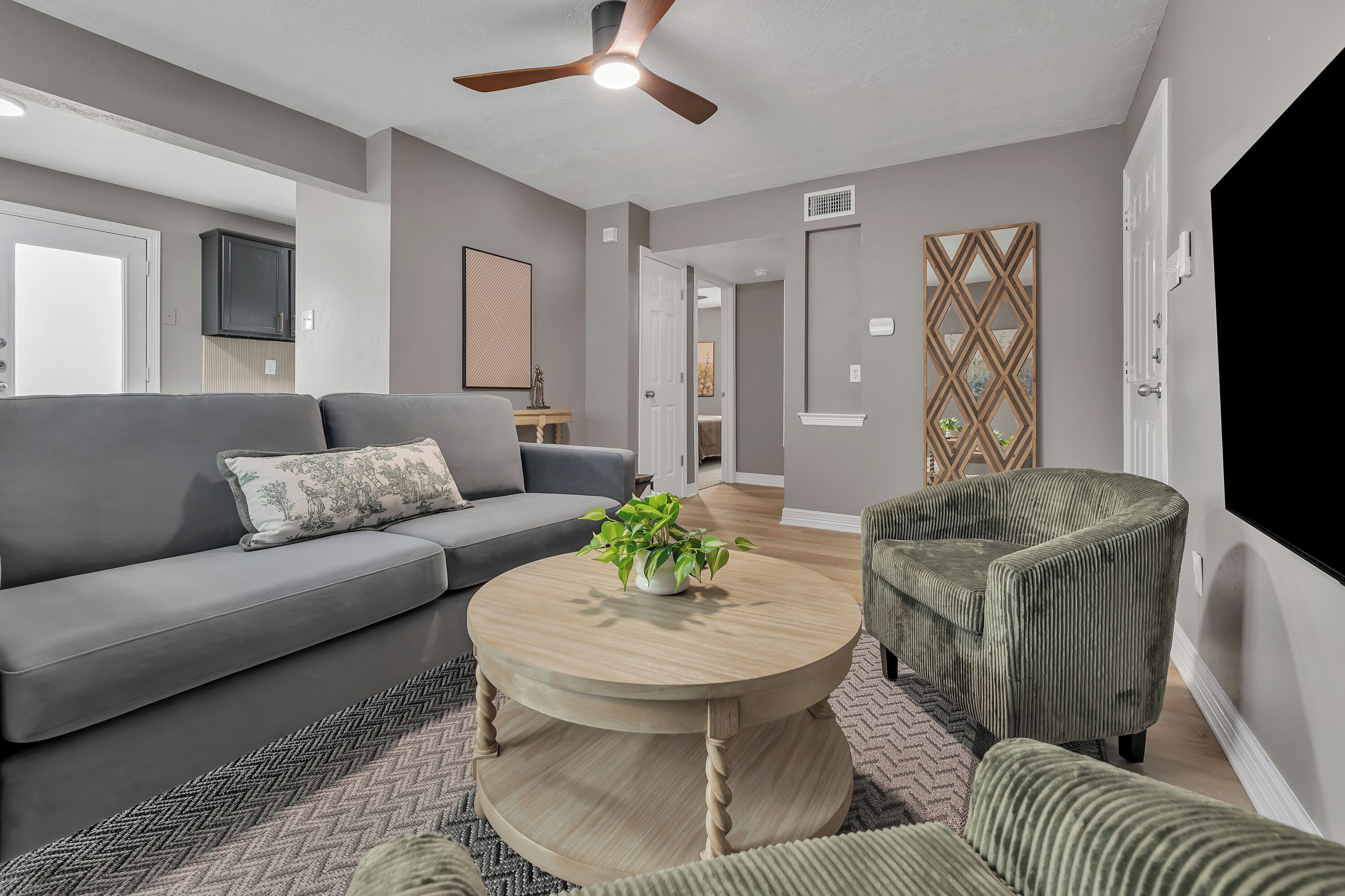 A modern living room with a grey sofa, a round wooden coffee table, a green armchair, and a ceiling fan.