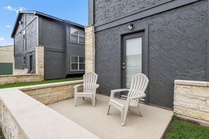 A two-story building with a stone facade and a dark grey exterior. There are two white plastic chairs on a concrete patio. - El Camino:Comfy King Beds-Walk to Campus/Northgate (Bryan)