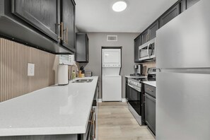 A kitchen with a white countertop, dark cabinets, a refrigerator, a microwave, and a stove. - El Camino:Comfy King Beds-Walk to Campus/Northgate (Bryan)