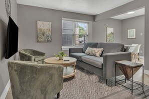 Ein Wohnzimmer mit grauem Sofa, zwei grünen Sesseln, einem runden Couchtisch und einem kleinen Beistelltisch.