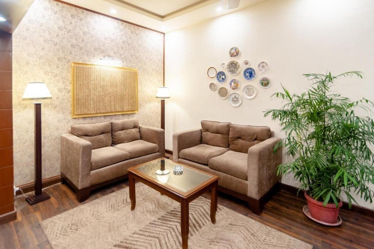 A living room with two sofas, a coffee table, a floor lamp, a wall-mounted decorative panel, and a potted plant.
