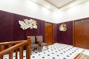 A reception area with a wooden staircase, two grey upholstered chairs, a decorative wall piece, and a large wooden door. - Shelton Guest House (Islamabad)