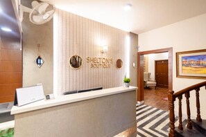 A reception desk with a sign reading 'Shelton's Boutique,' a wall-mounted fan, and a framed painting on the wall. - Shelton Guest House (Islamabad)