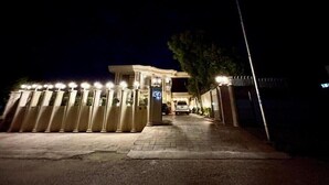 Una entrada protegida por una cancela, un cartel con un número y un camino que lleva a un edificio, con un vehículo estacionado en el interior.