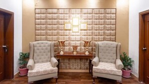 Una habitación con dos sillones, una mesa de madera con tres trofeos dorados y un papel tapiz con diseño.