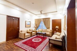 A living room with two sofas, a coffee table, a red patterned rug, and a ceiling fan. - Shelton Guest House (Islamabad)