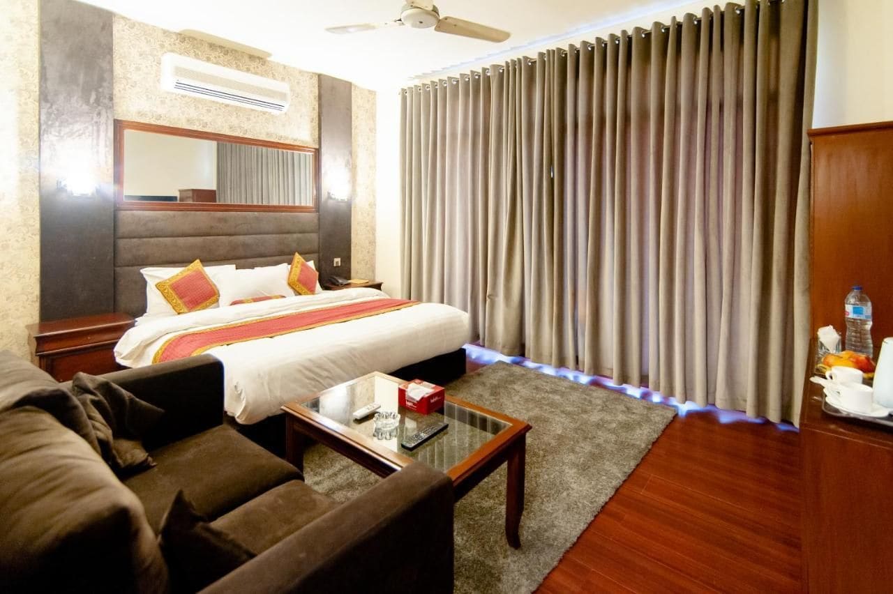 Una habitación de hotel con cama, sofá, mesa de centro, espejo y cortinas.