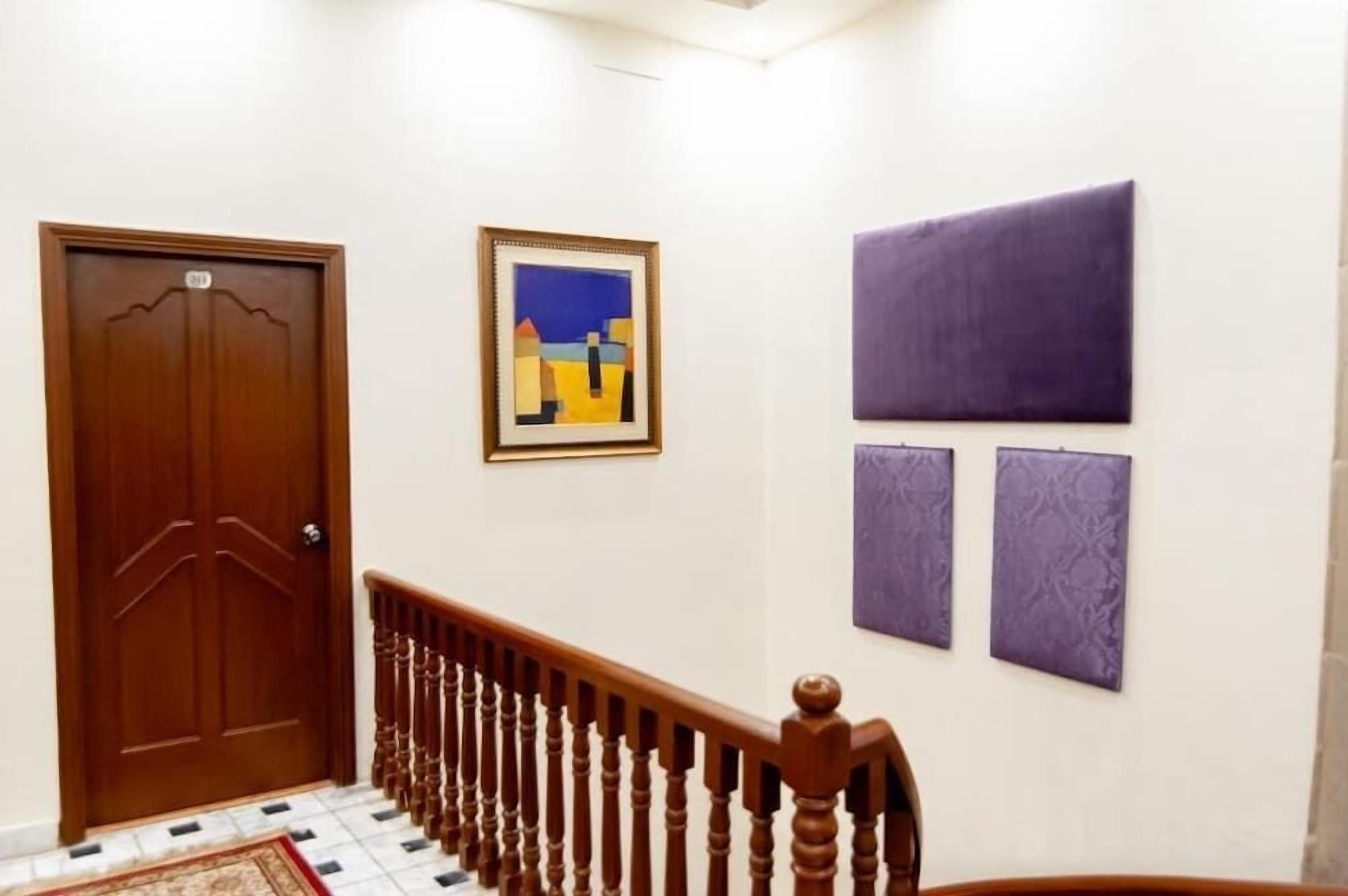 A hallway with a wooden door, a staircase with a wooden handrail, and three framed artworks on the wall.