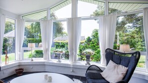 Una veranda con soffitto curvo, ampie finestre, un tavolo rotondo e una sedia in vimini.
