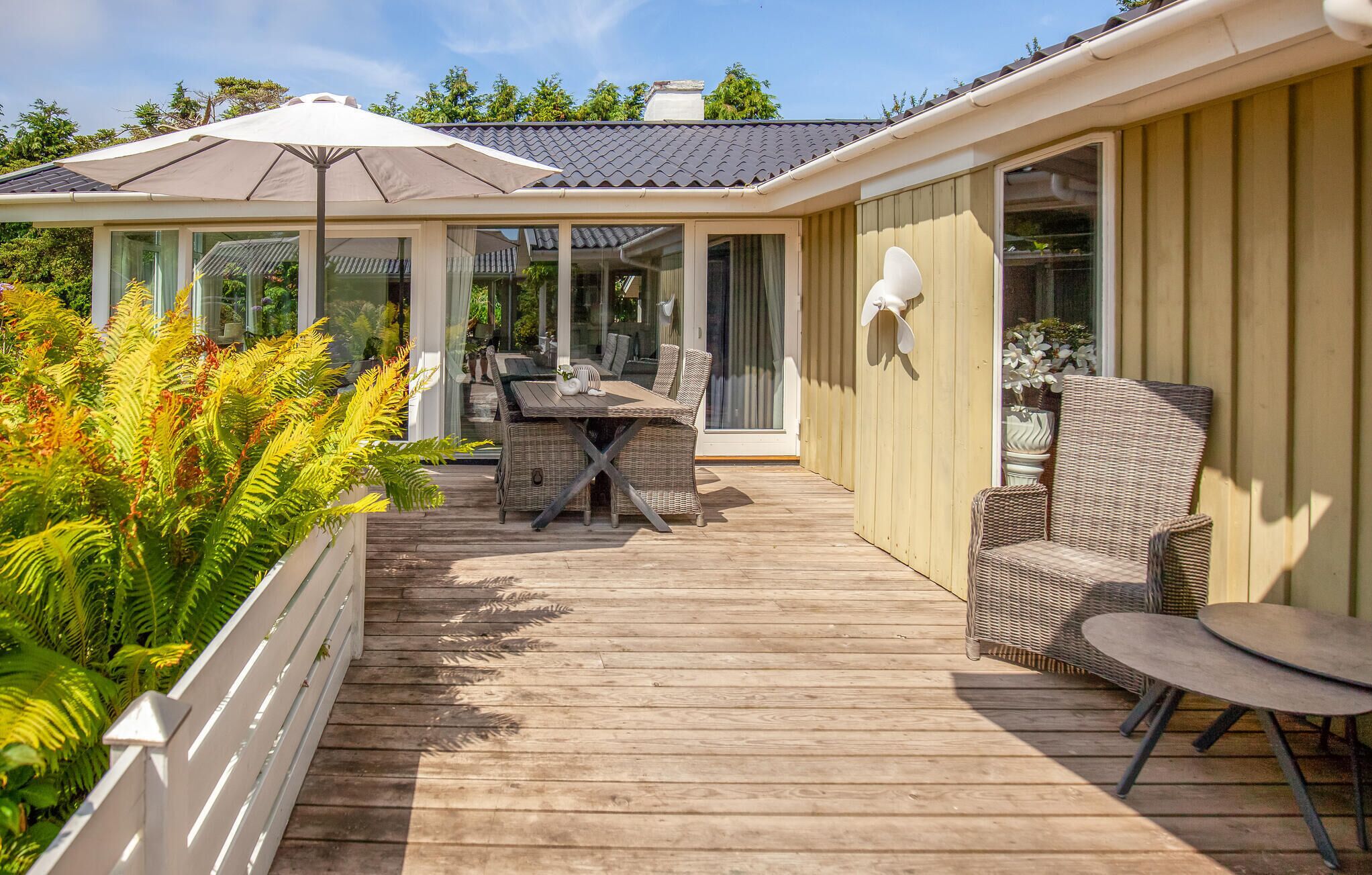 Een overdekt terras buiten met een eettafel en stoelen, omgeven door weelderige beplanting.