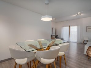 A modern dining area with a glass table and white chairs, a ceiling fan, and a view of a living room with a sofa and curtains. - Marina retreat with lake view (Lagos)