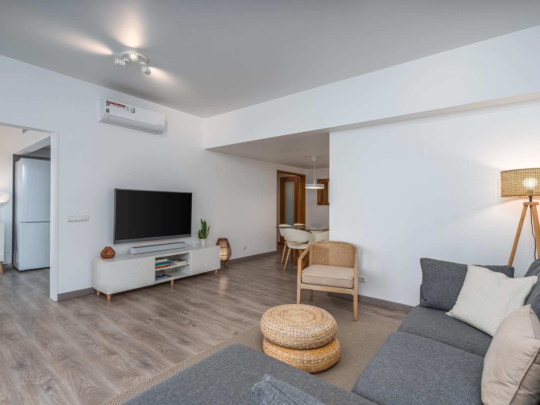 A modern living room with a flat-screen TV, a sofa, a dining area with chairs, and a floor lamp.