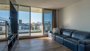 A modern living room with a large window, a leather sofa, and a flat-screen TV. - City and Park View Close to Station 1 Car Space (Beaconsfield)