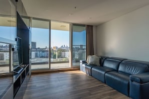 A modern living room with a large window, a leather sofa, and a flat-screen TV. - City and Park View Close to Station 1 Car Space (Beaconsfield)