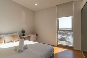 A modern bedroom with a large bed, a desk, and a view of the city through a large window. - City and Park View Close to Station 1 Car Space (Beaconsfield)