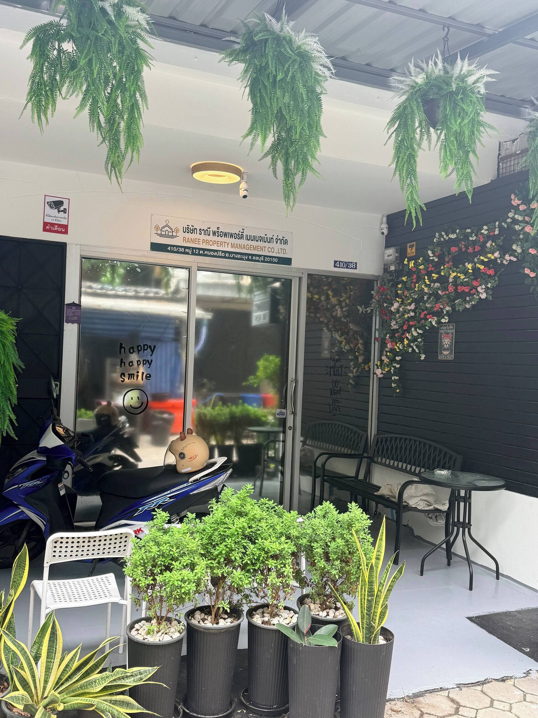 A property management company sign, a scooter, potted plants, and outdoor seating.