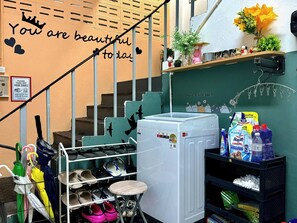 Una escalera con un letrero que dice 'You are beautiful today', un zapatero con varios zapatos, un taburete pequeño y un estante con productos de limpieza.