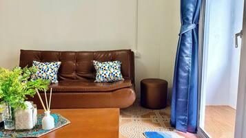 A brown leather sofa with two patterned pillows, a wooden coffee table with a decorative mat, a small round ottoman, and a patterned rug.