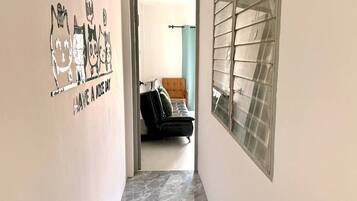 A hallway with a wall mural, a window with blinds, and a glimpse of a room with a couch.