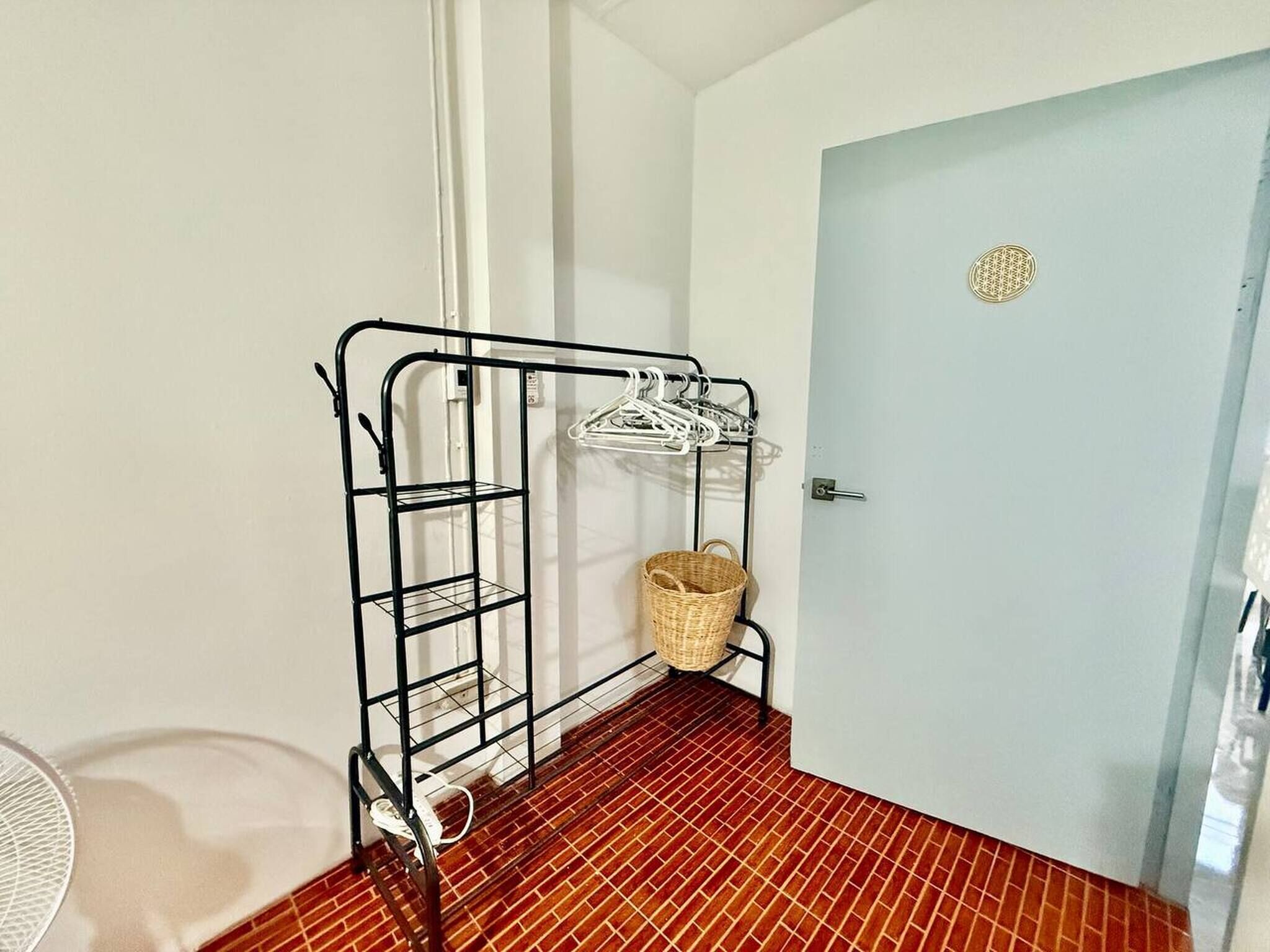 A room with a metal rack holding clothes, a wicker basket, and a door with a circular decoration.