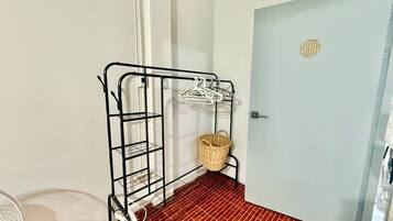 A room with a metal rack holding clothes, a wicker basket, and a door with a circular decoration.