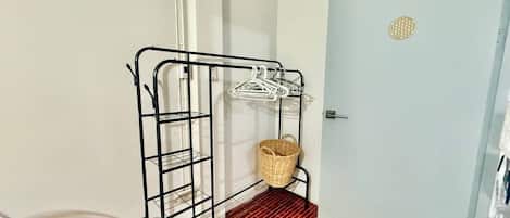 A room with a metal rack holding clothes, a wicker basket, and a door with a circular decoration.