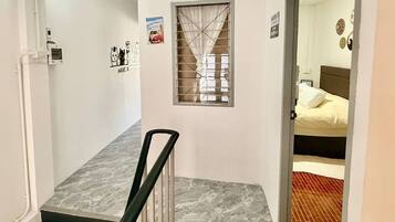 A hallway with a marble floor, a window with a curtain, and a bed with a white pillow in the adjacent room.