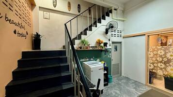 A staircase leading to a landing with a wall-mounted fan, a small plant, and a sign with a heart symbol.