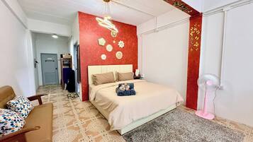 A hotel room with a bed, a chair, a desk, a wall with decorative items, and a ceiling fan.