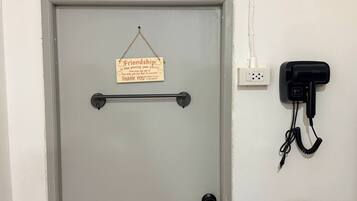 A grey door with a sign that reads 'Friendship is like pissing your pants! Everyone can see it, but only you can feel its warmth. THANK YOU!' A black telephone is mounted on the wall to the right.
