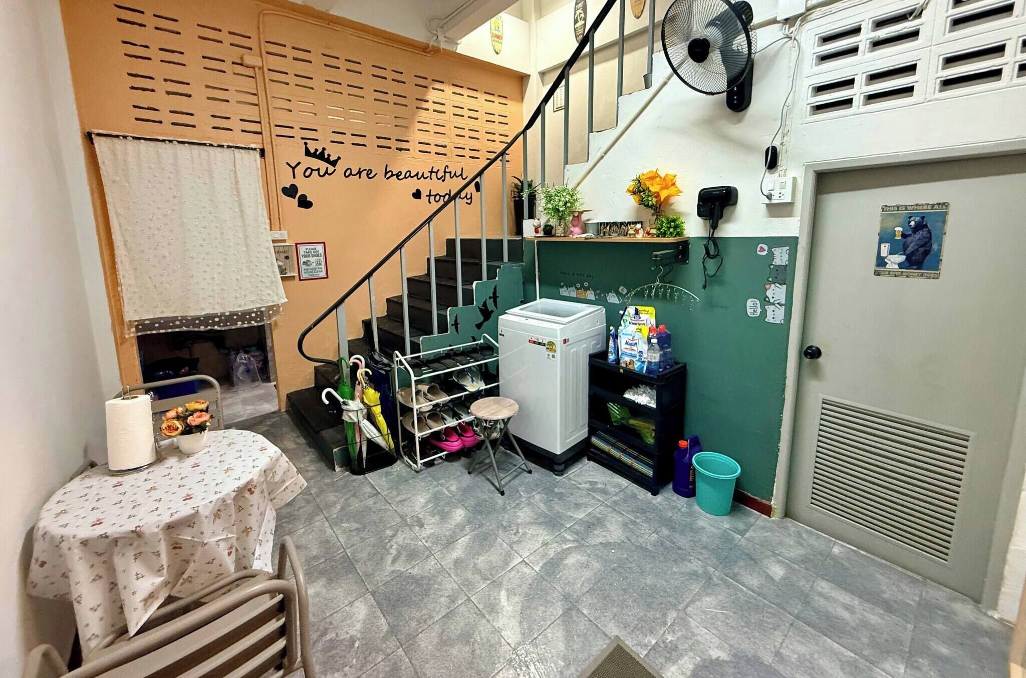 A small room with a staircase, a table with a floral tablecloth, a fan, and a refrigerator.