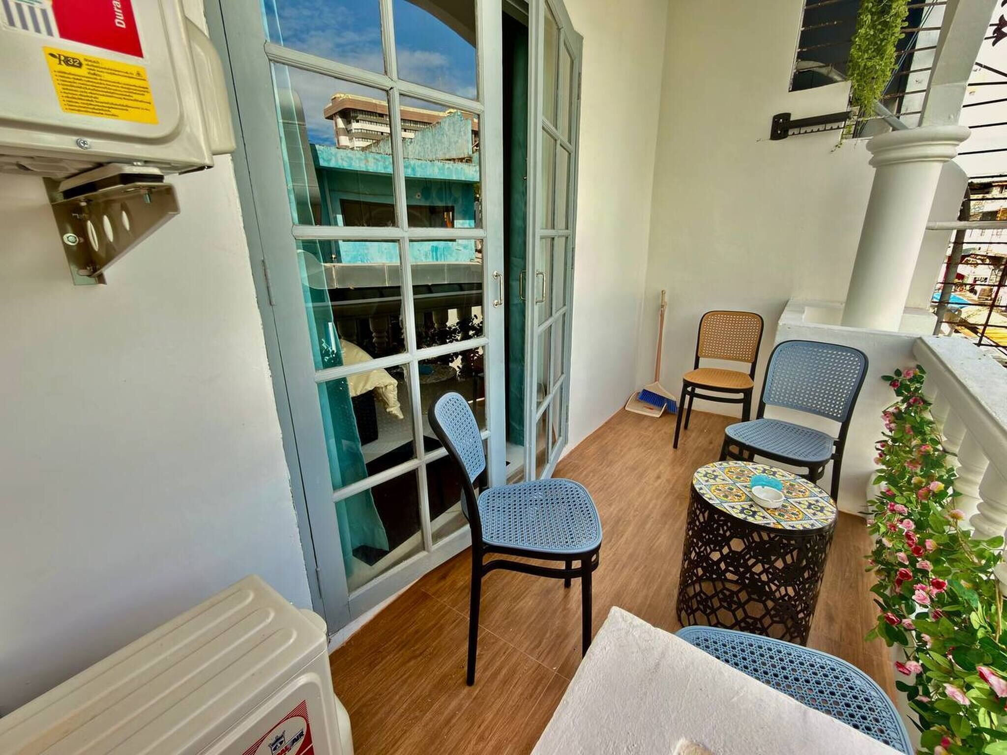 A balcony with a view of a building, two chairs, a small table, and a broom.