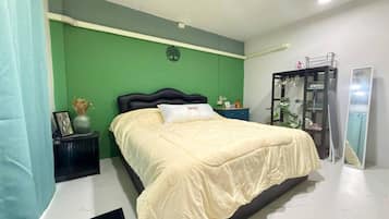 A bedroom with a bed, a nightstand, a dresser, a mirror, and a green wall.
