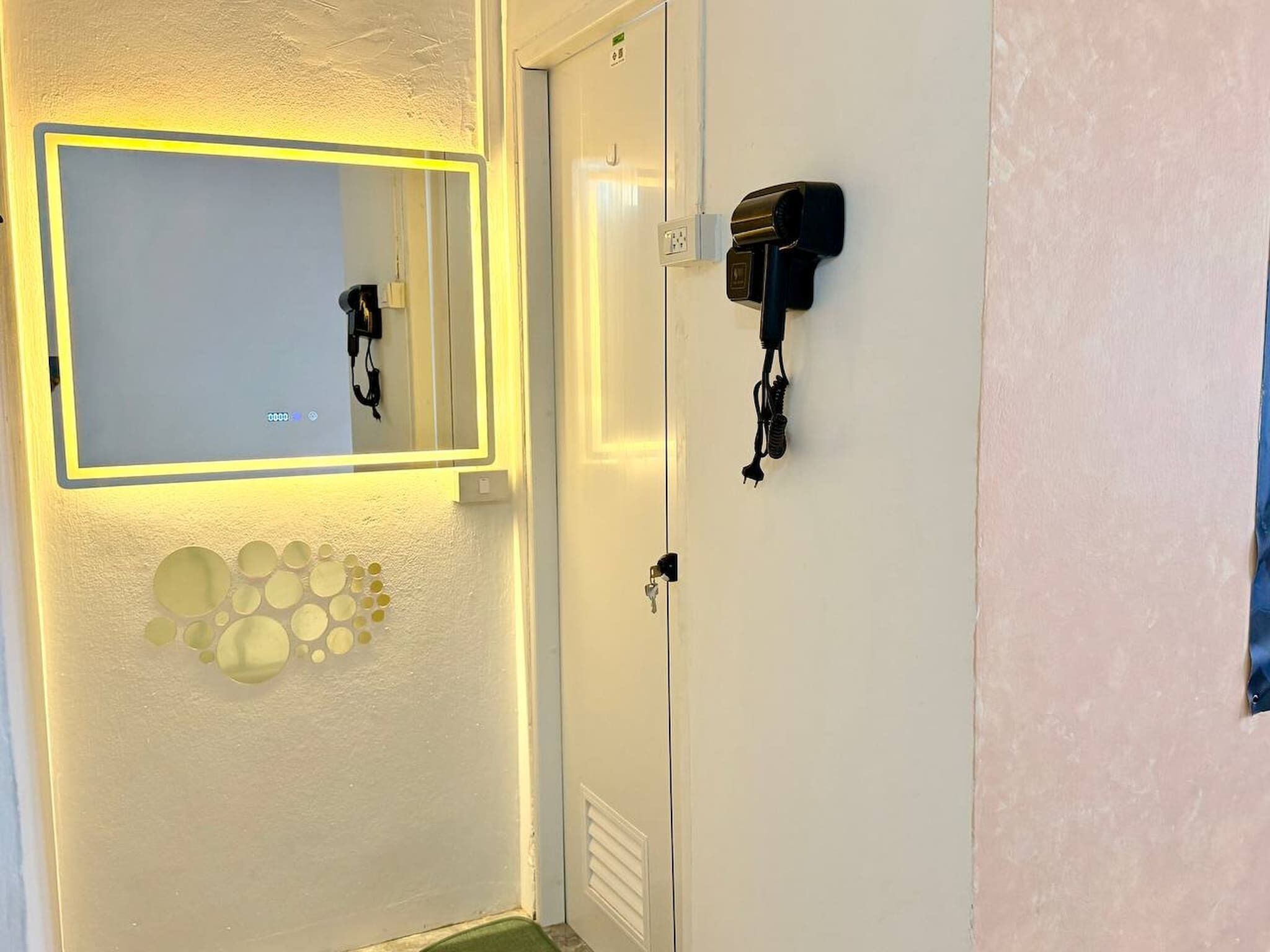 A room with a mirror, a wall-mounted hairdryer, and a door with a handle.
