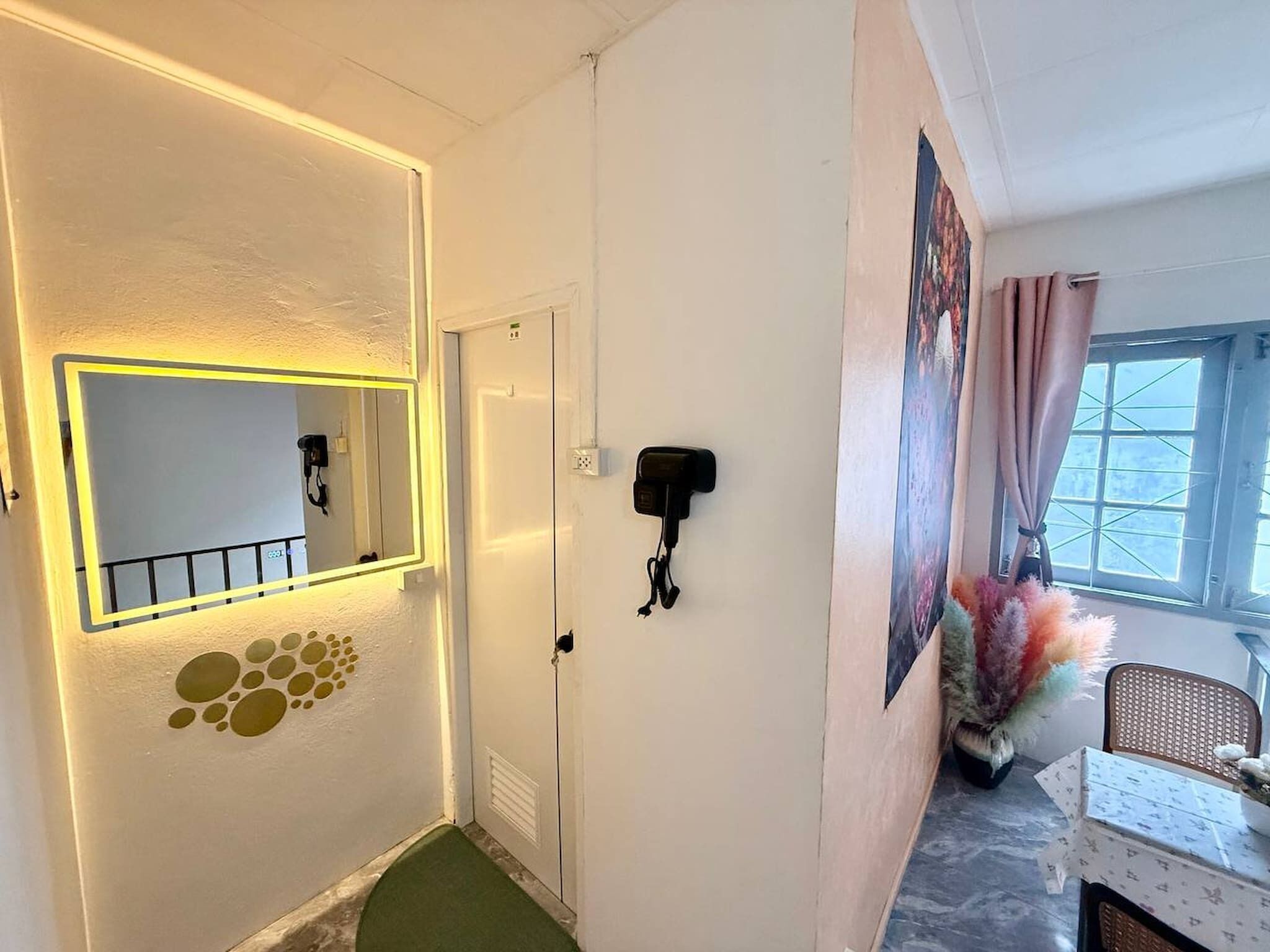 A hallway with a mirror, a door, a wall-mounted phone, and a window with curtains.