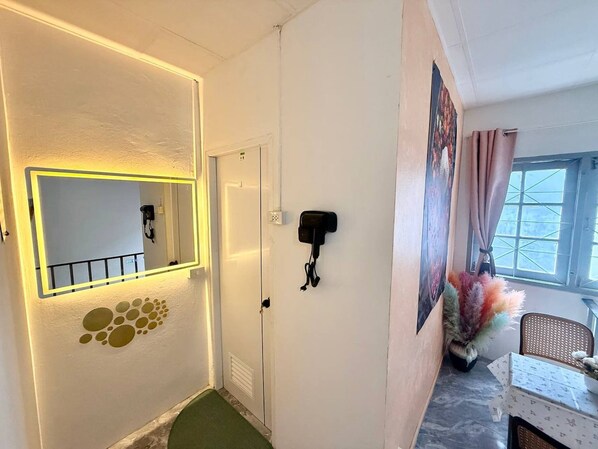 Un pasillo con espejo, una puerta, un teléfono en la pared y una ventana con cortinas.