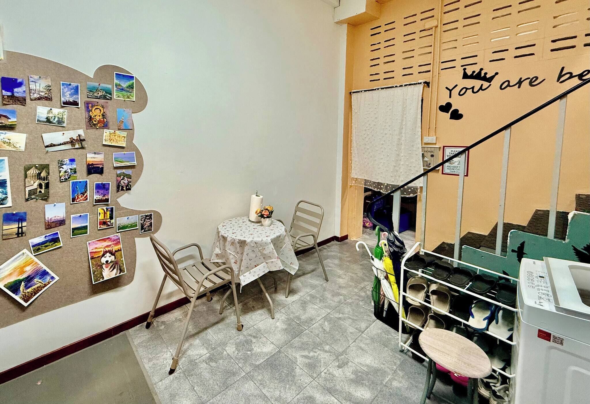A small dining area with a table and chairs, a bulletin board with photos, and a staircase with a sign.