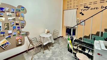 A small dining area with a table and chairs, a bulletin board with photos, and a staircase with a sign.
