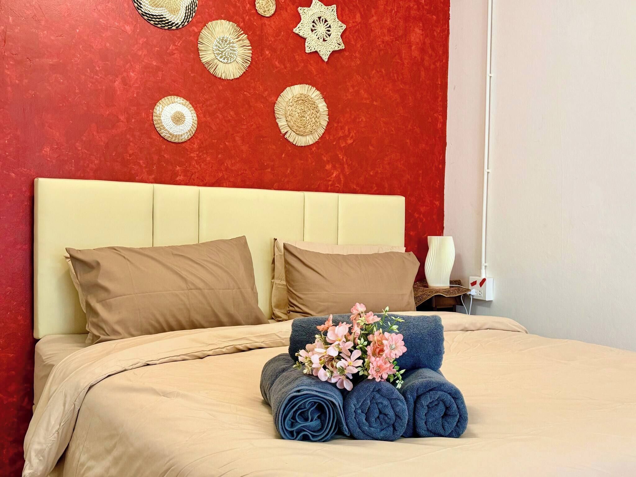 En seng med beige sengetøj, to puder, et natbord med en lampe og en væg med dekorative vævede genstande.