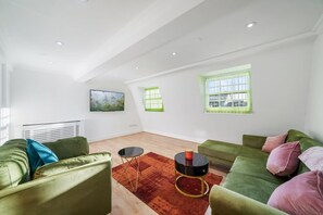 Ein geräumiges Wohnzimmer mit grünen Sofas, einem schwarzen Couchtisch und einem roten Teppich.