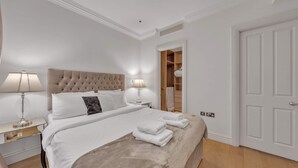 Ein Schlafzimmer mit einem großen Bett, zwei Nachttischlampen, einem Holz-Kopfteil, einem Kleiderschrank mit Spiegel und einer weißen Tür.